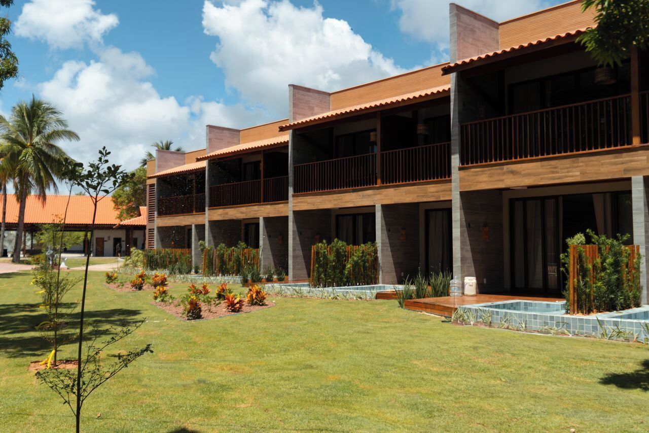 Ein modernes Hotel mit mehreren Balkonen, einem gepflegten Garten und blauem Himmel.