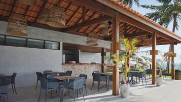 An outdoor dining area with wicker hanging lights, a concrete floor, and a view of the ocean.