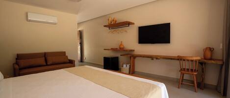 Habitación de hotel con una cama grande, un sofá, un escritorio con una silla, un televisor de pantalla plana y una mesita con un florero.