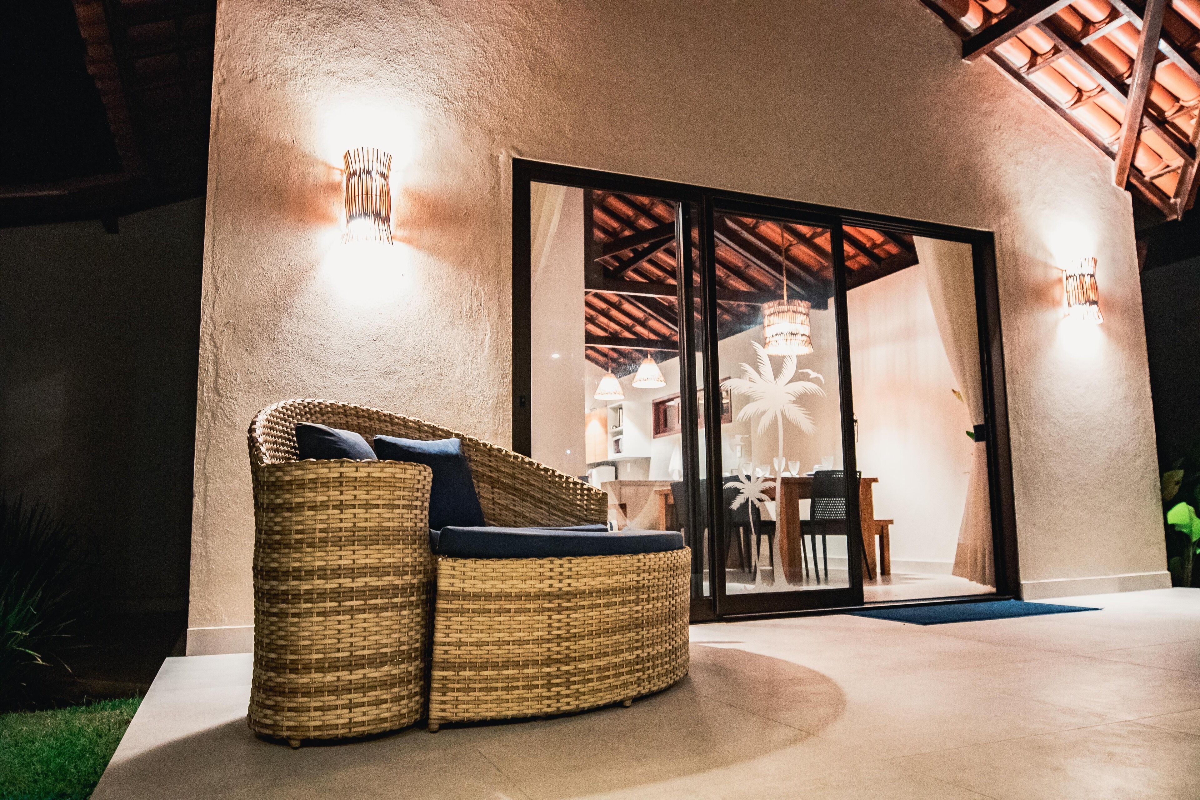 A wicker sofa with cushions outside a building with a glass door, a concrete floor, and a ceiling with wooden beams.