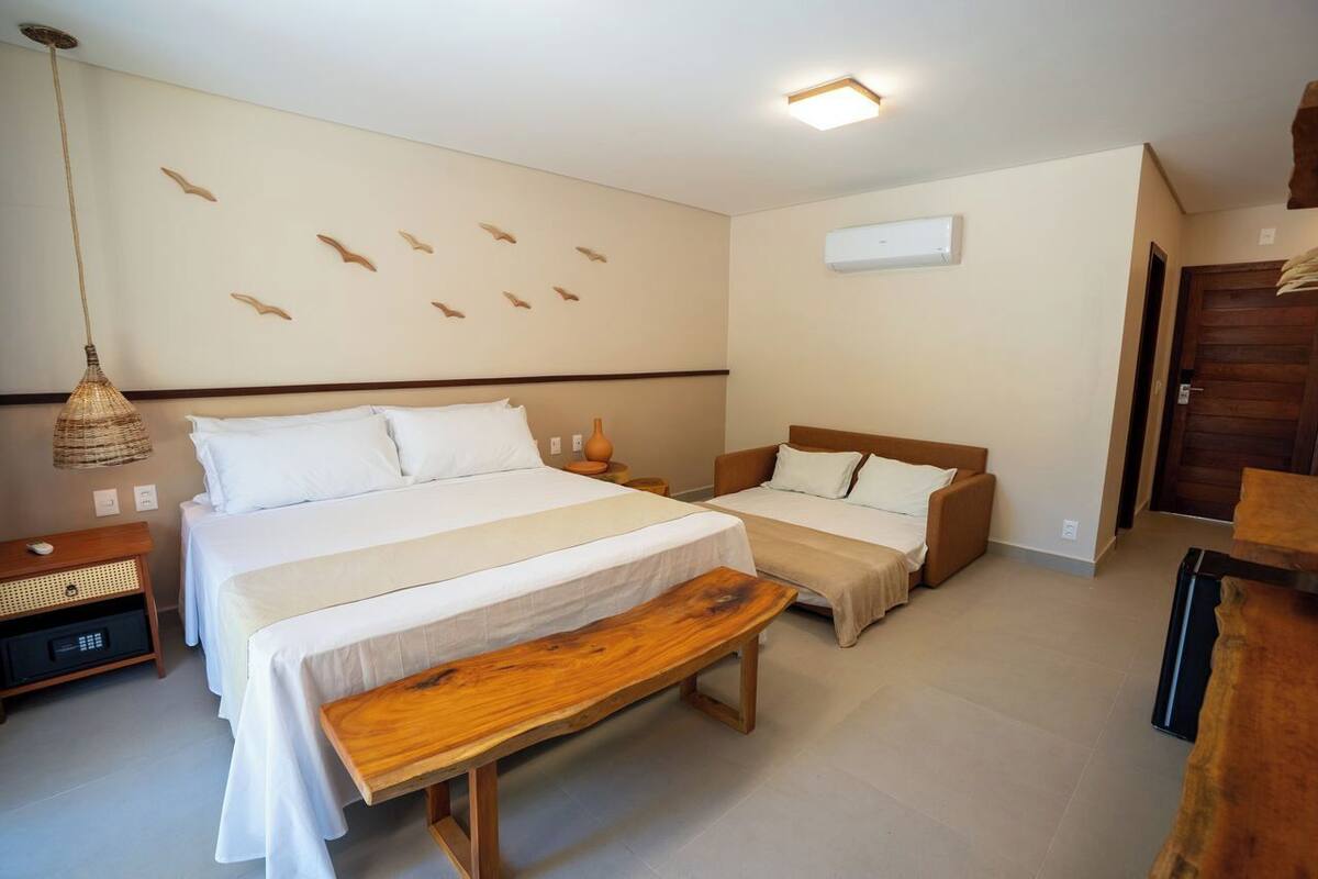 A bedroom with two beds, a bench, a bedside table, a hanging lamp, and a wall-mounted air conditioner.