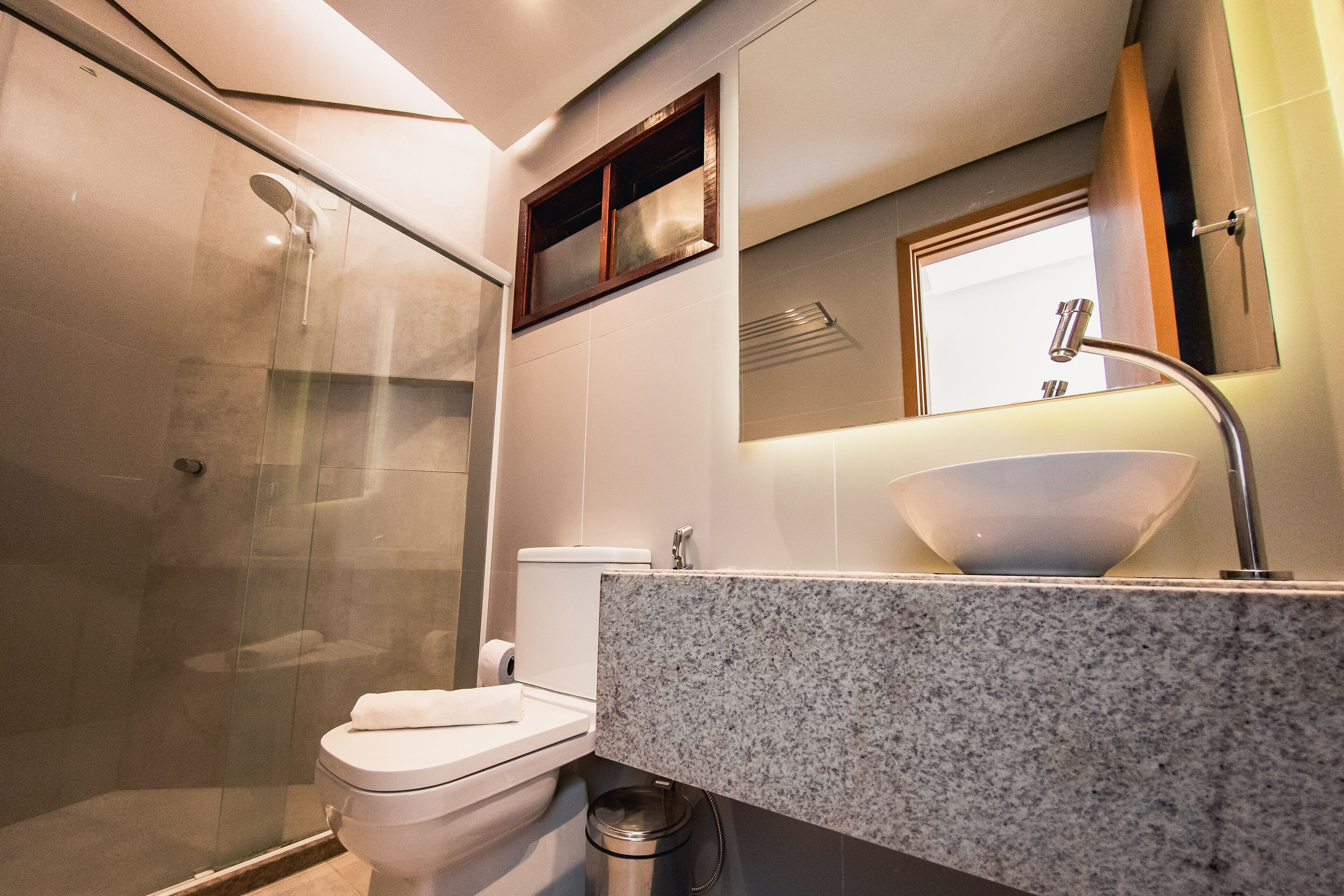 A modern bathroom with a glass shower enclosure, a white toilet, and a granite countertop with a vessel sink.