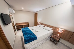 Una habitación de hotel moderna con una cama grande, una mesita de noche, un televisor montado en la pared y un cabecero de madera.