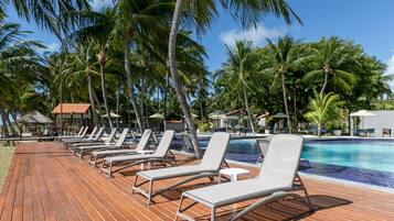 Un área junto a la piscina con sillones de descanso y palmeras.