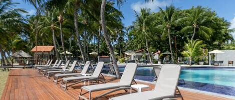 Un área junto a la piscina con sillones de descanso y palmeras.