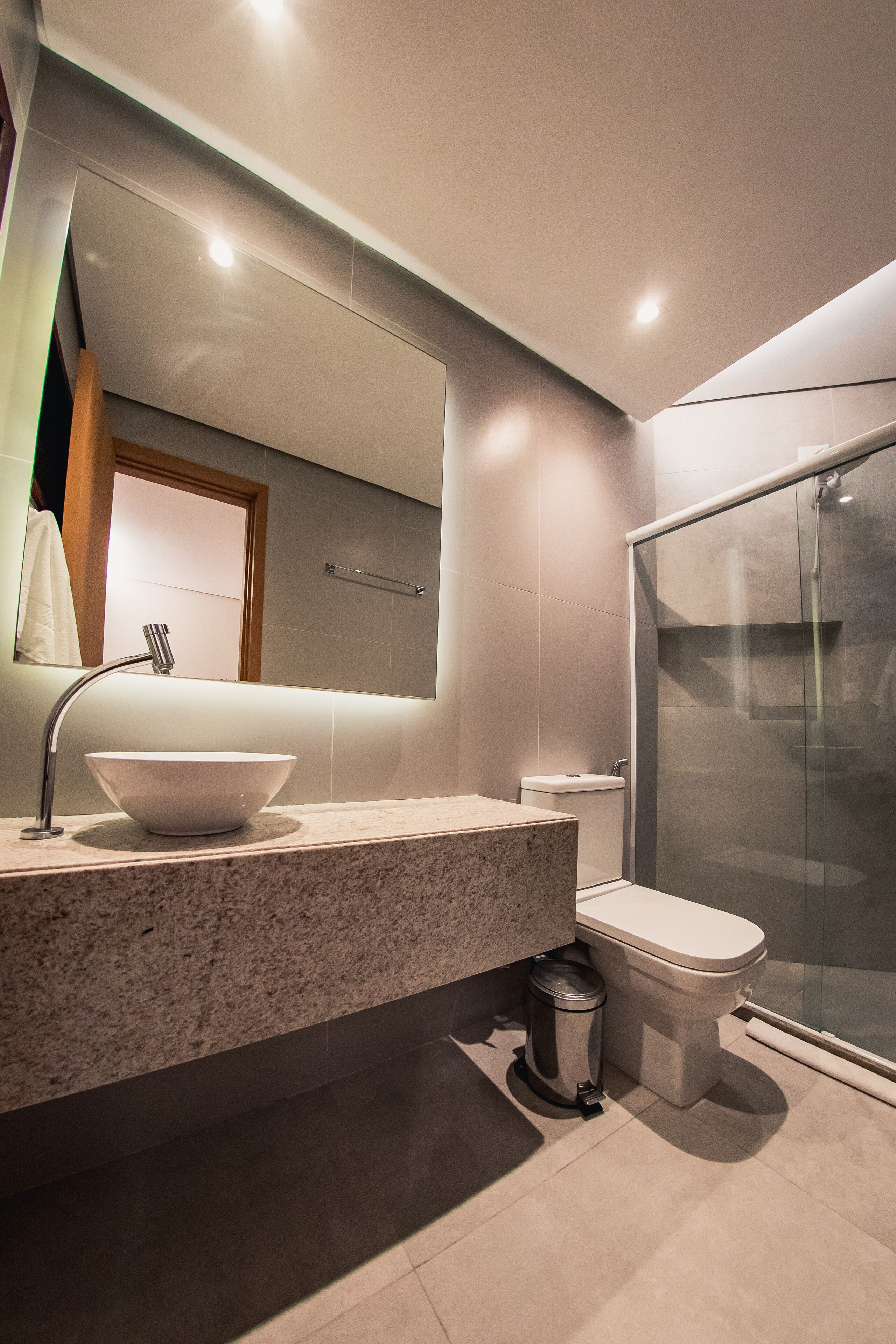 A modern bathroom with a large mirror, a vessel sink, a toilet, and a glass shower enclosure.