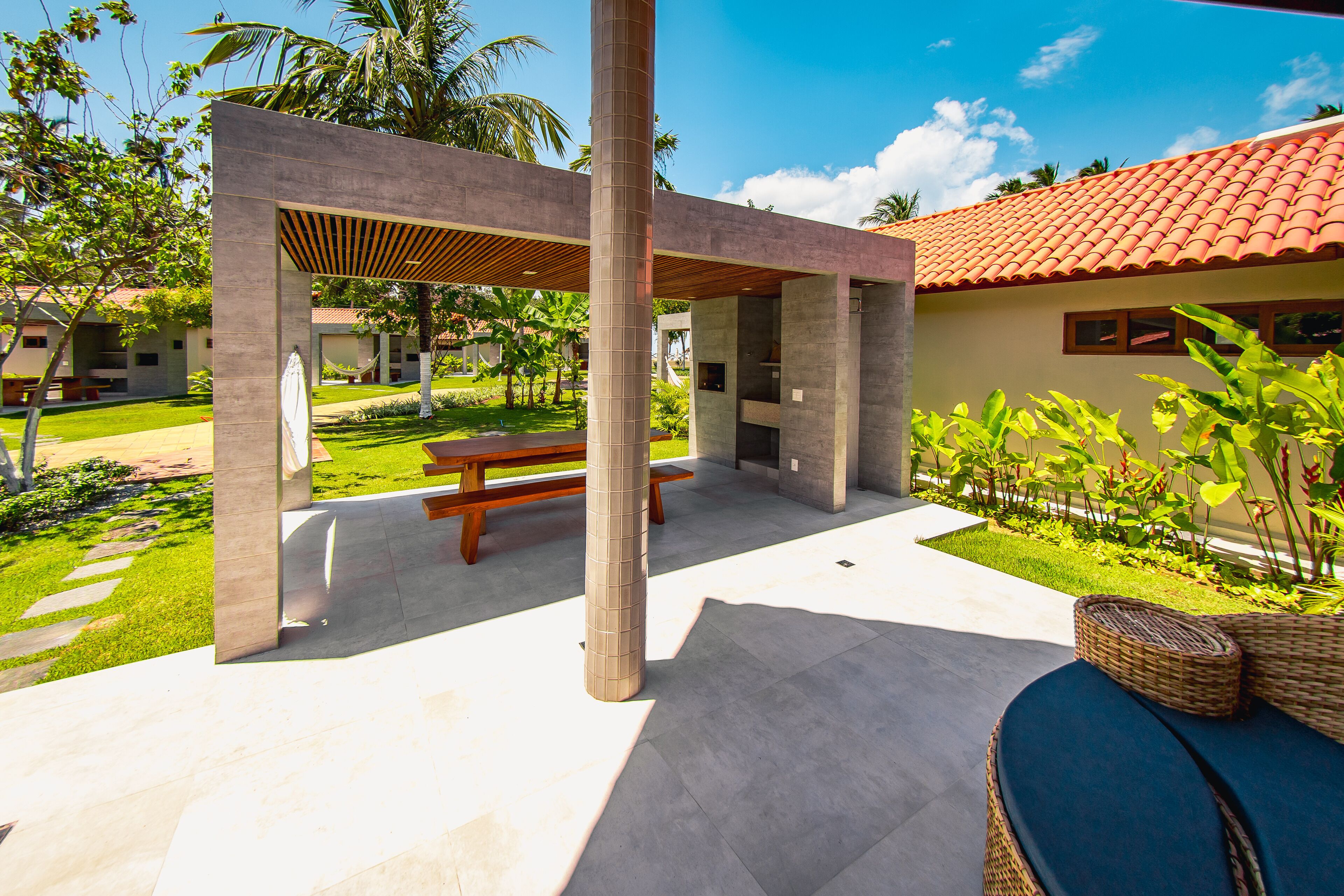 A covered outdoor area with a picnic table, a pergola, and a lounge area with wicker furniture.