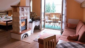 A cozy living room with a fireplace, a sofa, a dining table, and a balcony with outdoor seating. - Penzion Lampaš (Poprad)