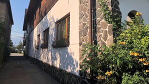 A traditional building with stone walls and wooden beams, featuring windows with flower boxes and a stone pathway leading to a gate. - Penzion Lampaš (Poprad)