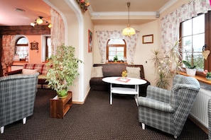 A cozy living room with a sofa, two plaid chairs, a round table, and a potted plant. - Penzion Lampaš (Poprad)
