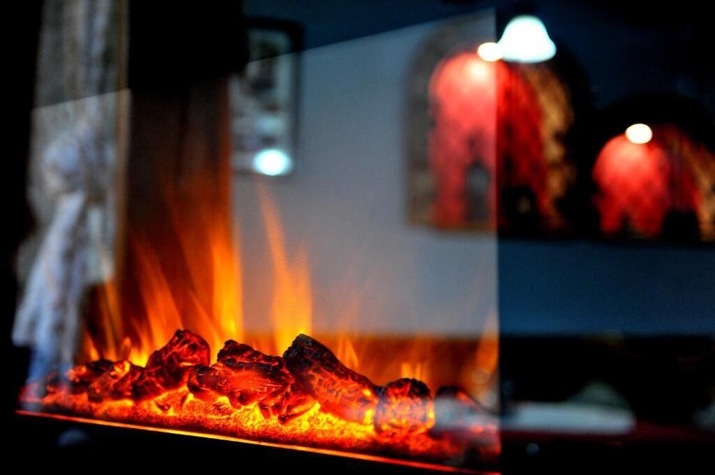Primer plano de una parrilla con carbón encendido, llamas visibles y una partición de cristal que refleja un interior borroso.