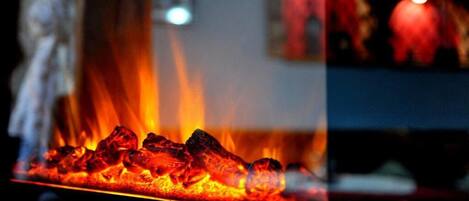 Primer plano de una parrilla con carbón encendido, llamas visibles y una partición de cristal que refleja un interior borroso.