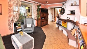 A cozy living room with a checkered sofa, a small table with a vase, and a fireplace with a fire. - Penzion Lampaš (Poprad)