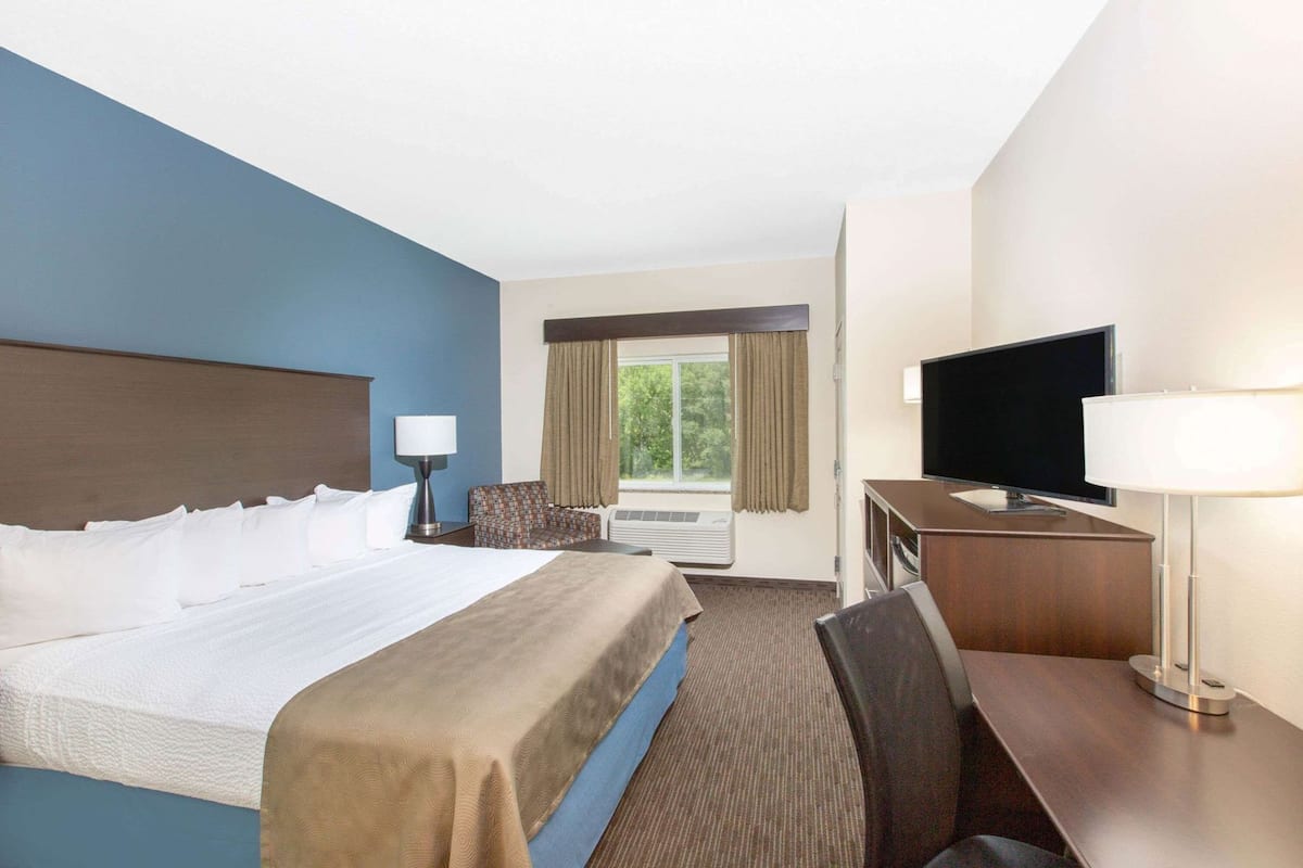 A hotel room with a large bed, a desk with a TV, a chair, and a window with curtains.