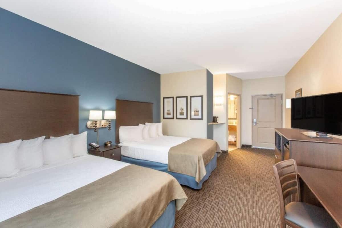 A hotel room with two beds, a desk, a television, and framed pictures on the wall.