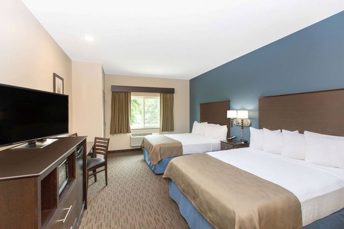 A hotel room with a TV, two beds, a desk with a chair, and a window with curtains.