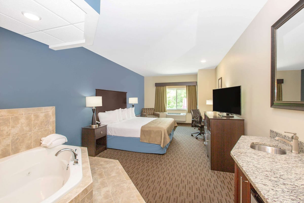 A hotel room with a large bed, a separate bathroom with a bathtub, a desk, and a television.