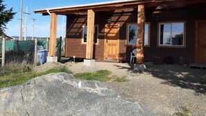 A wooden cabin with a porch, a door, and a window. - Cabañas Cerro Las Piedras (Punta Arenas)