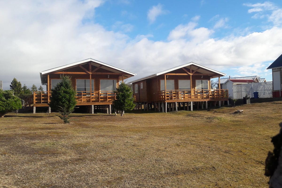 Two wooden cabins with balconies, a grassy field, and a clear sky.