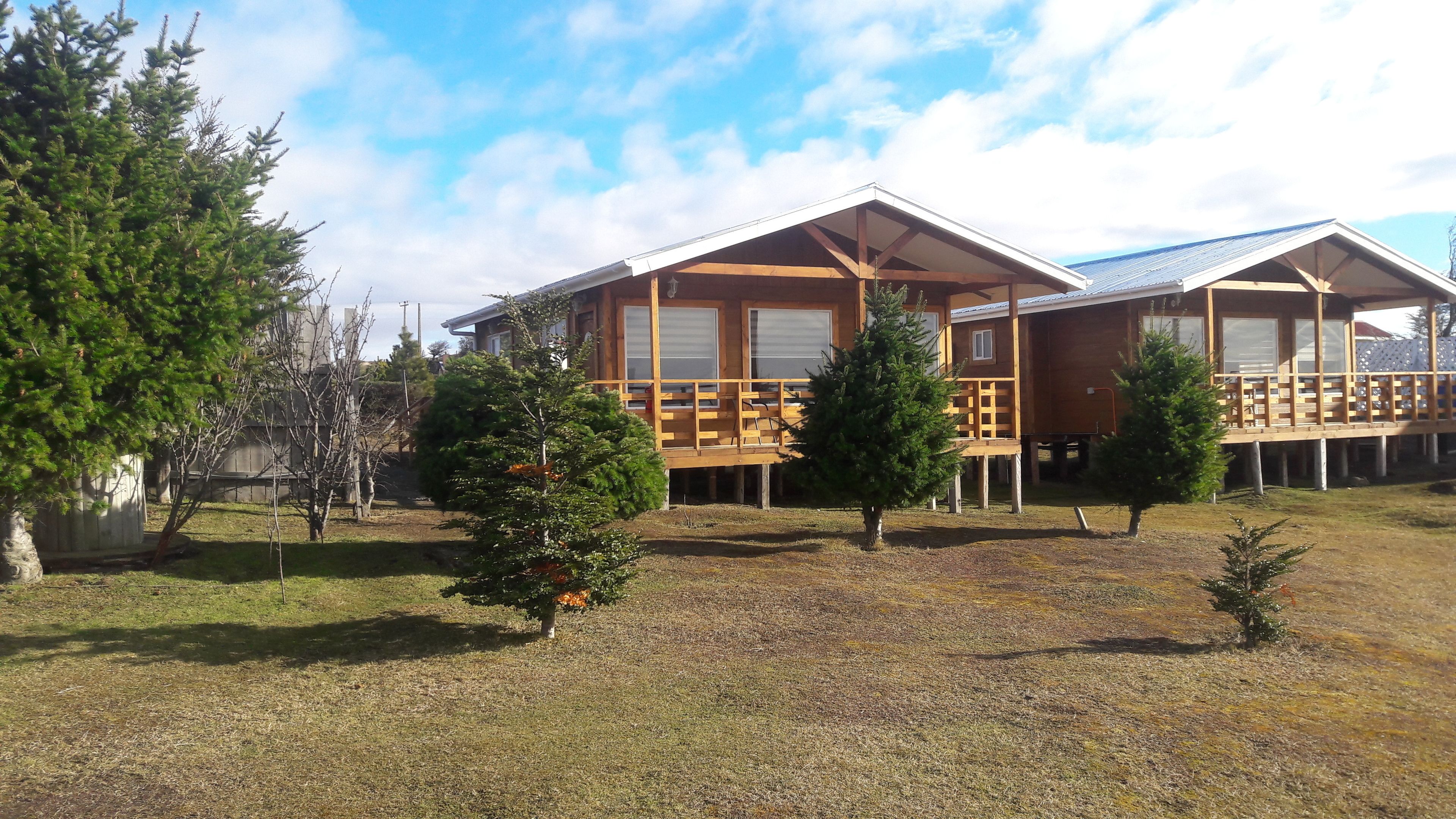 A two-story wooden cabin with a deck, surrounded by trees and a grassy yard.