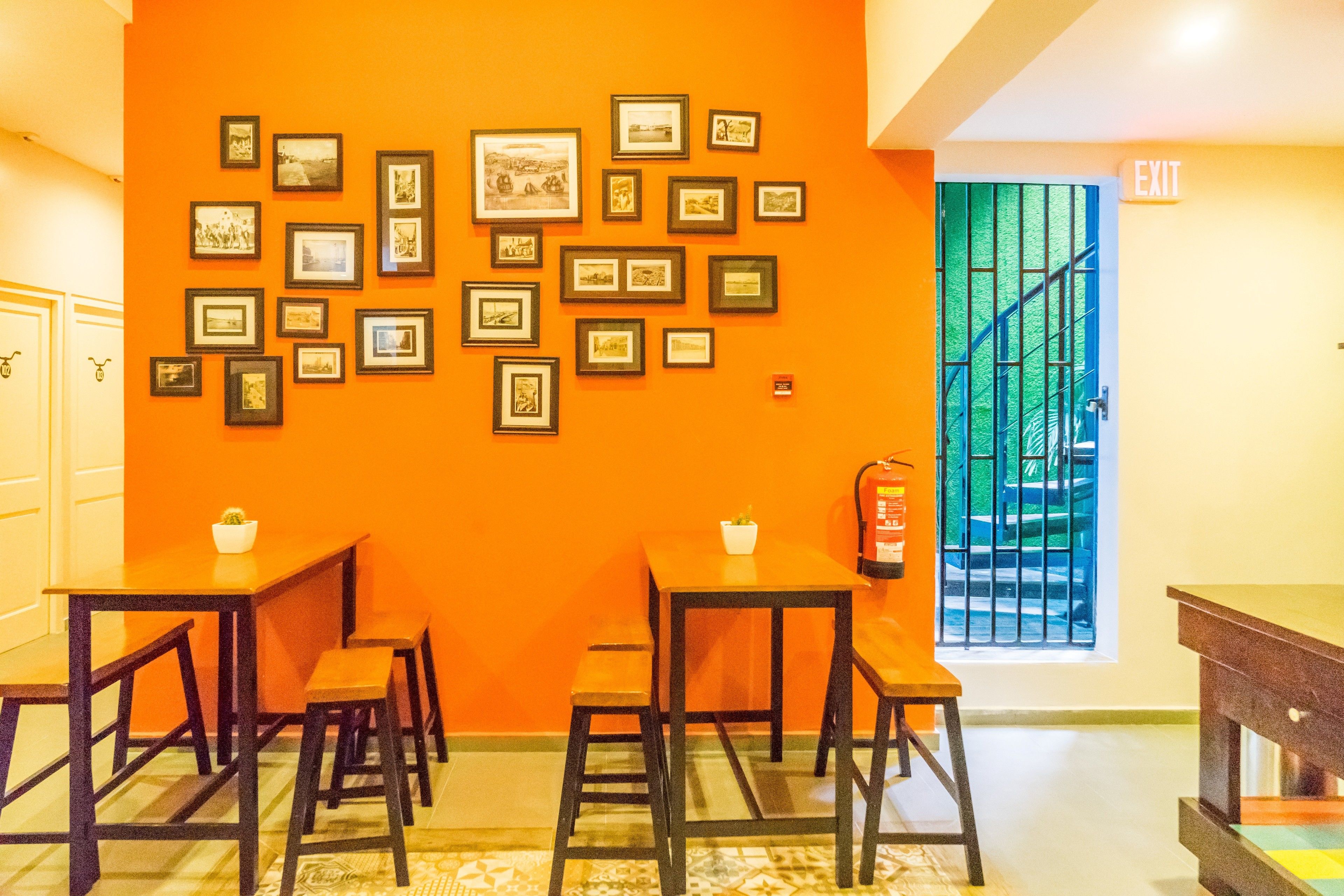 Een kamer met oranje wanden, meerdere ingekaderde foto’s aan de muur, en een trap die naar een uitgang leidt.