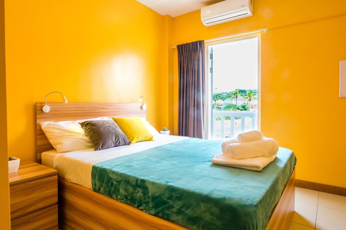 Ein Hotelzimmer mit Bett, Holz-Kopfteil und Blick ins Freie durch ein Fenster.