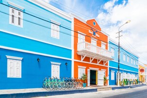 A brightly colored hotel with a blue and orange facade, a balcony, and bicycles parked outside.