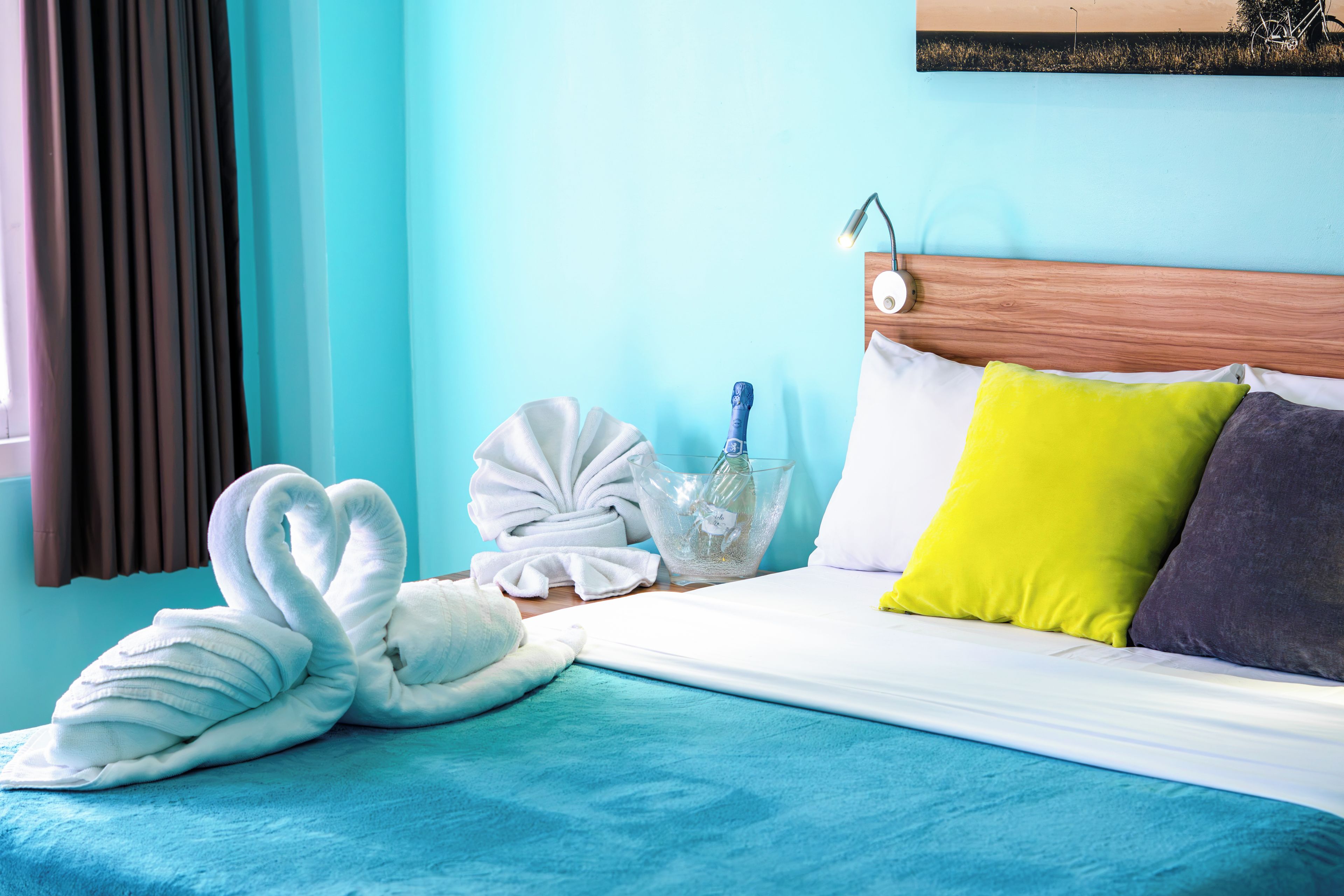 A neatly made bed with a blue bedspread, a wooden headboard, and pillows in yellow and gray.