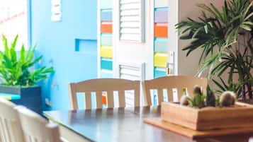 A dining area with a wooden table and chairs, a potted plant, and a colorful wall with shutters.