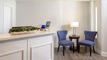 A reception area with a counter, two blue upholstered chairs, a small table with a lamp, and a laptop on the counter.
