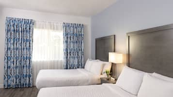 Habitación de hotel con dos camas, una mesita de noche con lámpara y una ventana con cortinas estampadas.