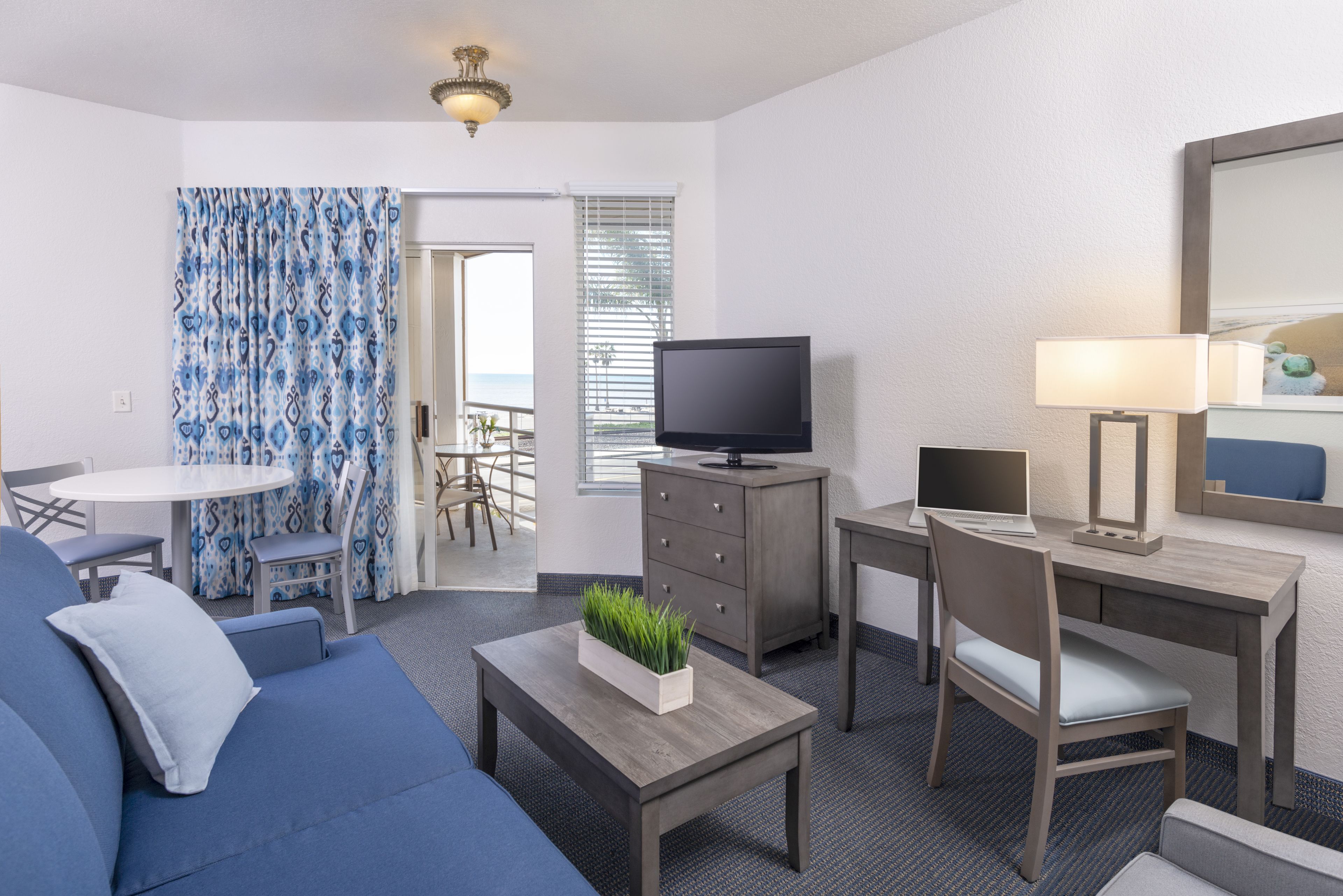 A modern hotel room with a sofa, a TV, a desk, and a dining area.
