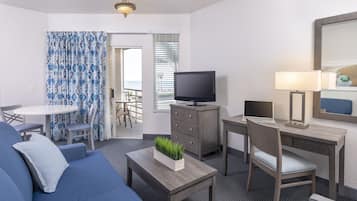 A modern hotel room with a sofa, a TV, a desk, and a dining area.