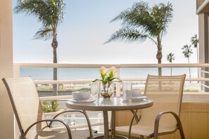 A balcony with a table set for two, overlooking a beach with palm trees. - Beachfront Inn and Suites at Dana Point (Dana Point)