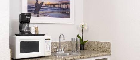 A kitchenette with a coffee maker, microwave, sink, and a framed picture of a pier.