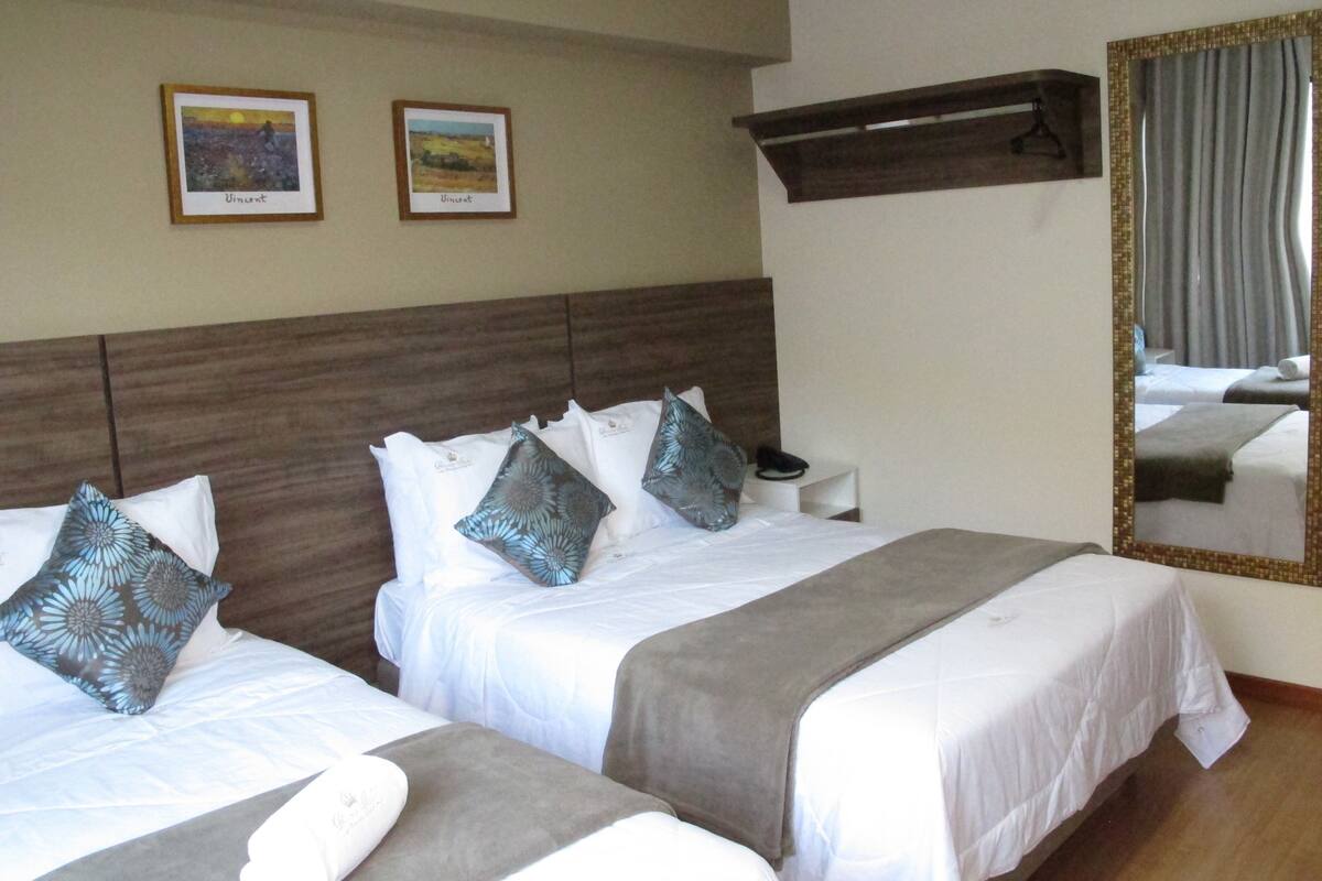 A hotel room with two beds, each with white bedding and decorative pillows. There are two framed artworks on the wall above the beds.