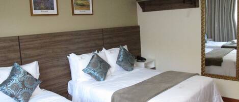 Habitación de hotel con dos camas, cada una con ropa de cama blanca y almohadas decorativas. Dos obras de arte enmarcadas adornan la pared sobre las camas.