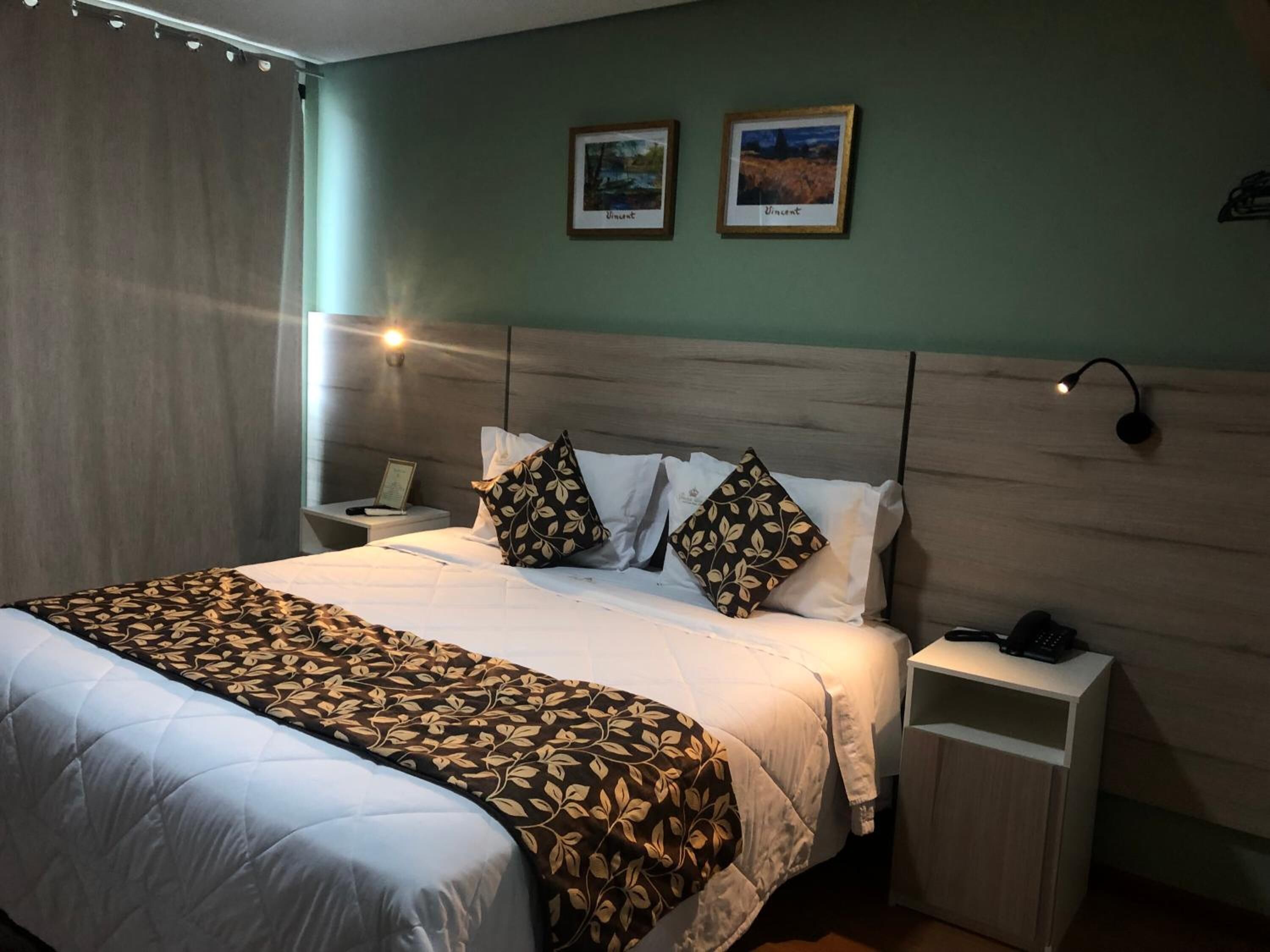 A neatly made bed with a patterned bedspread, a bedside table with a lamp, and two framed pictures on the wall.
