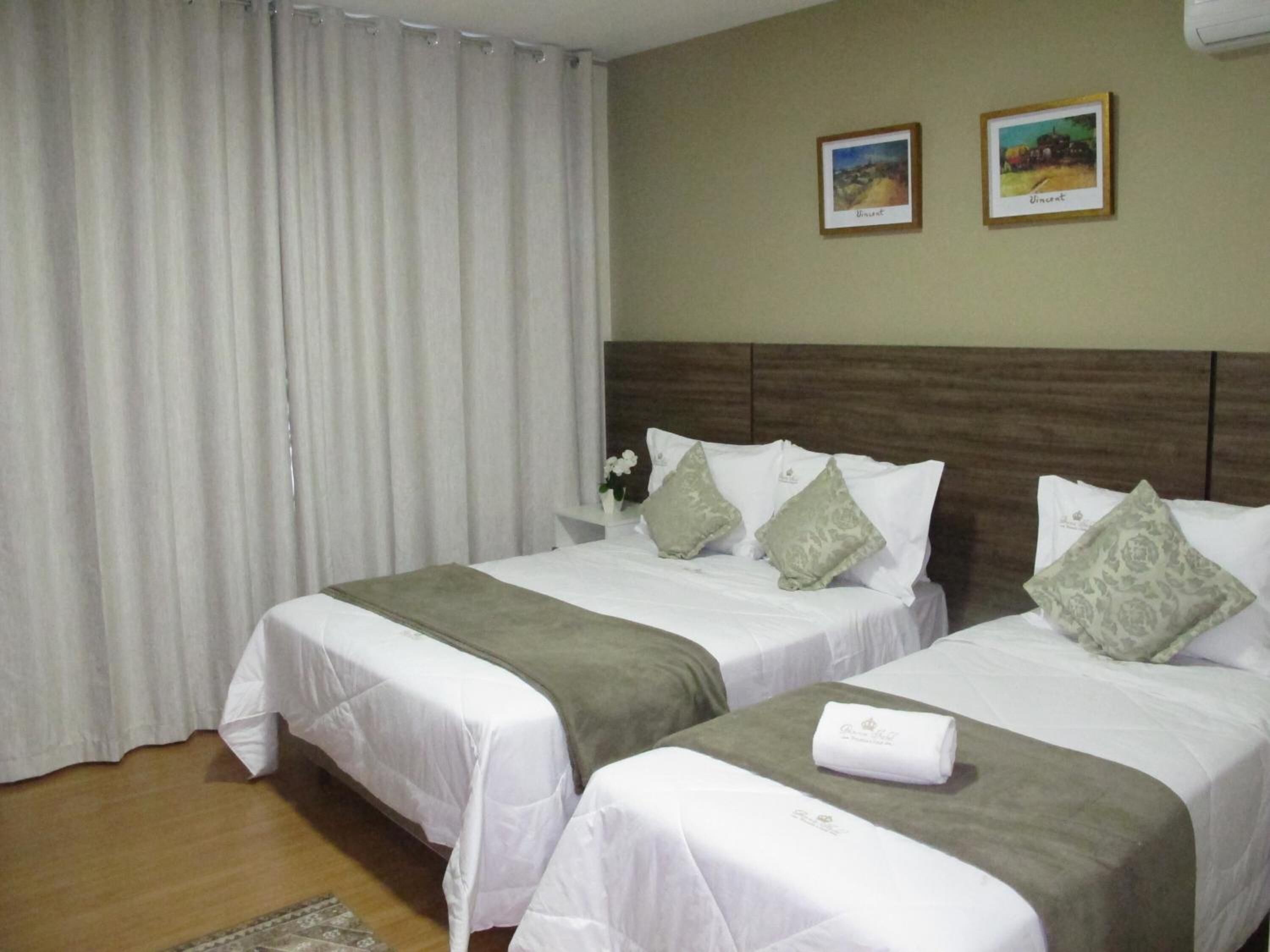 Habitación de hotel con dos camas, ropa de cama blanca, cabecera de madera y dos cuadros enmarcados en la pared.