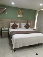 Un dormitorio ordenado con una cama, dos almohadas, una mesita de noche con un teléfono y un cuadro en la pared.