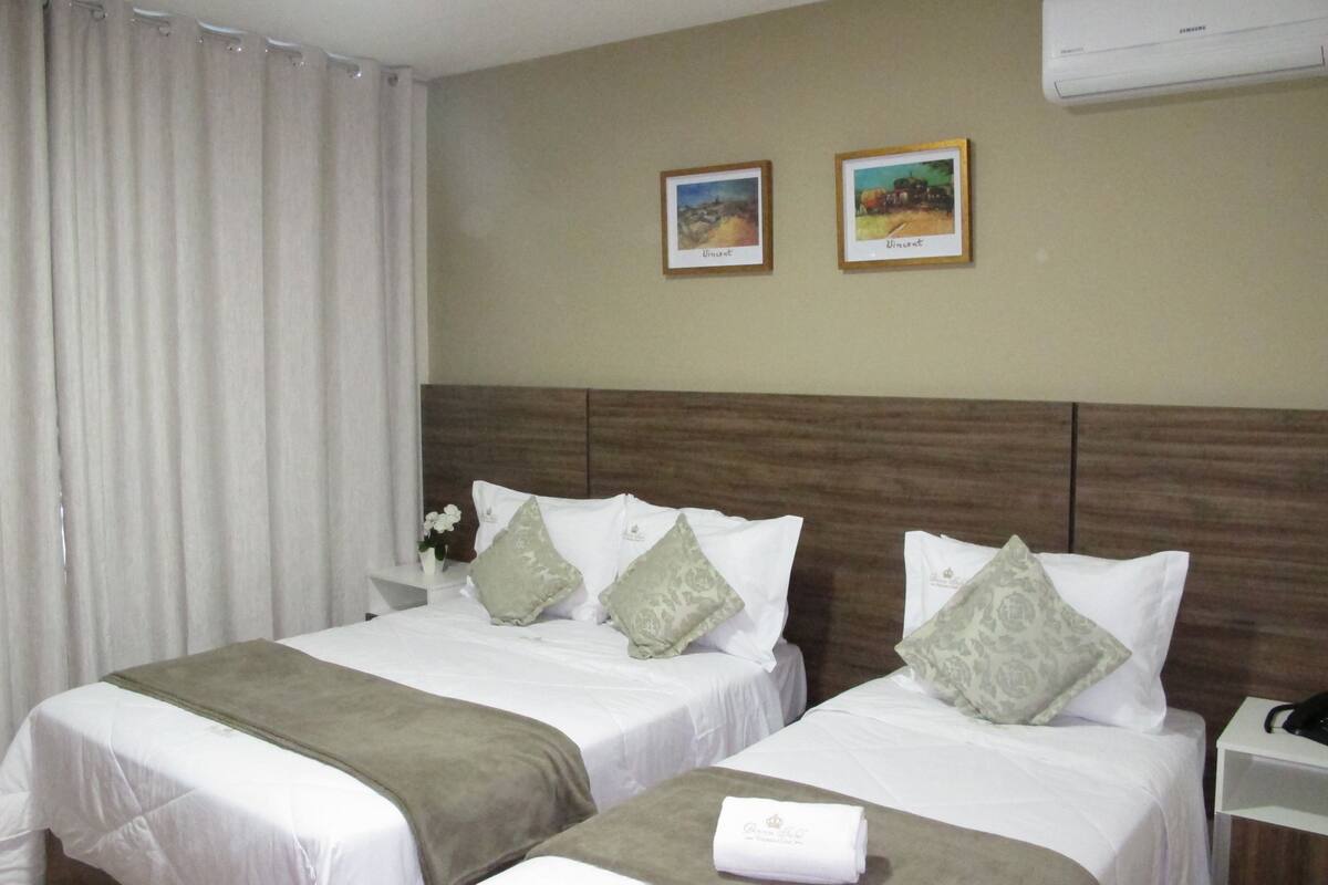 A hotel room with two beds, a wooden headboard, a nightstand with a phone, and two framed pictures on the wall.