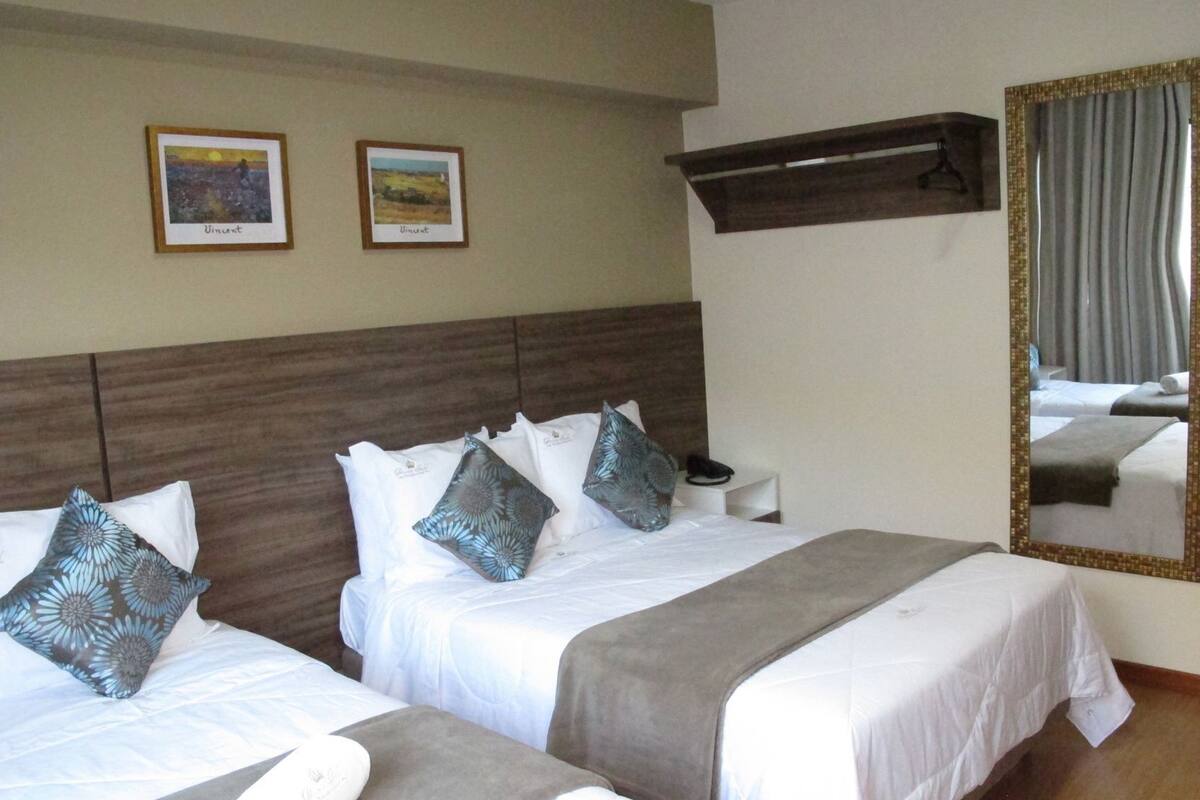 A hotel room with two beds, a wooden headboard, a mirror, and two framed pictures on the wall.