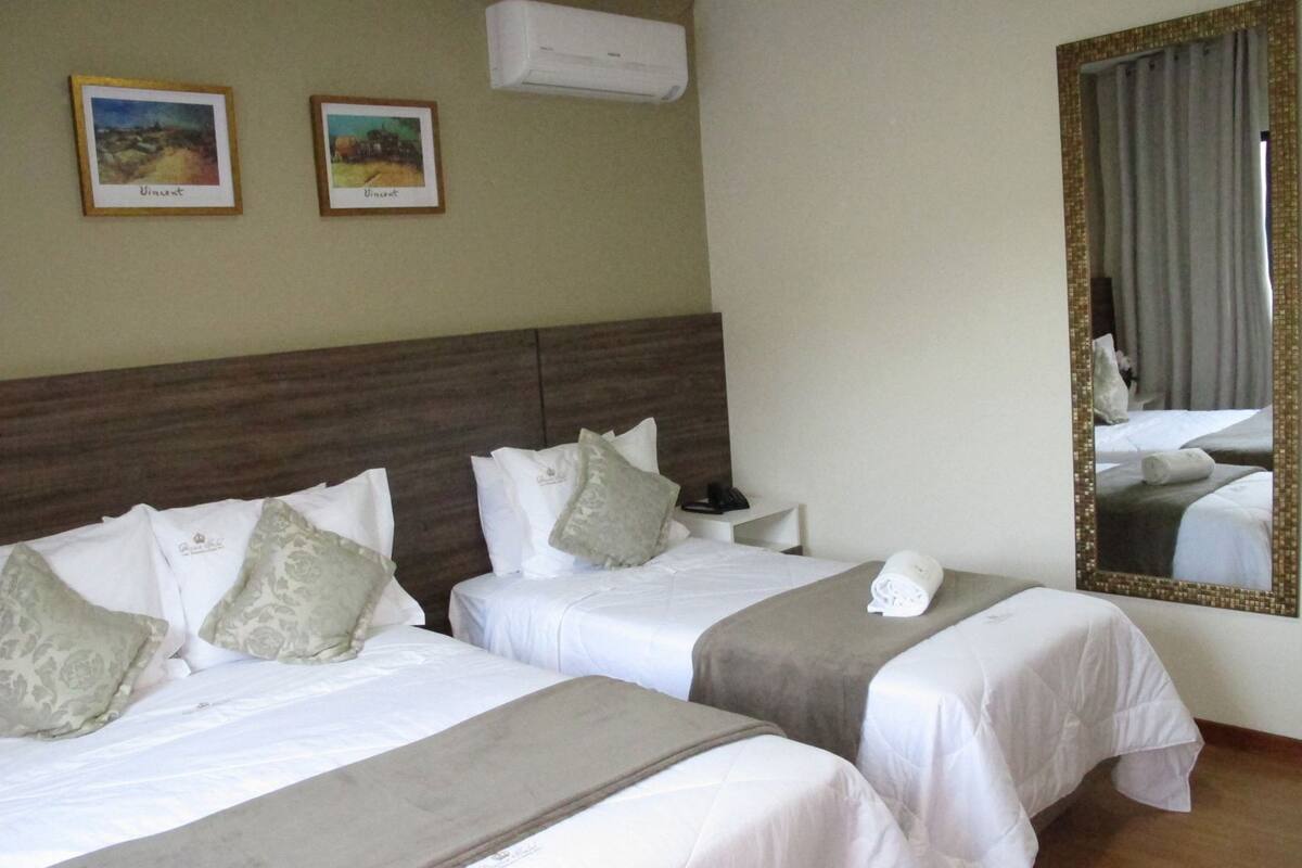 A hotel room with two beds, a nightstand, a mirror, and two framed pictures on the wall.