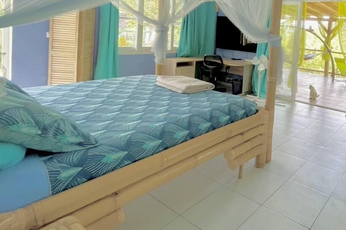 A room with a four-poster bed, a desk with a chair, and a view of the outdoors.