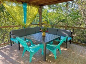 An outdoor seating area with a table and chairs, surrounded by a wooden deck and a view of greenery. - Maison d'hôtes Chez Adé Guadeloupe (Le Gosier)
