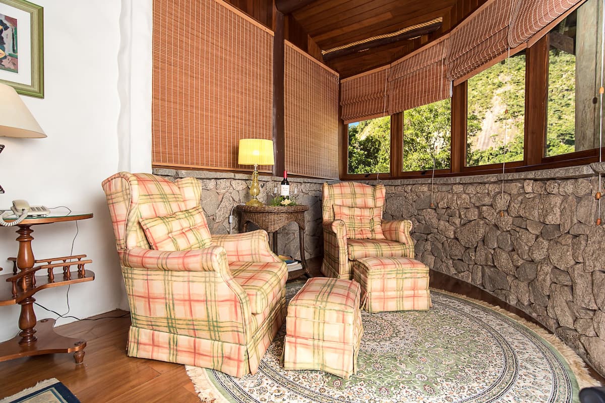 A cozy room with plaid furniture, a stone wall, and a view of greenery outside.