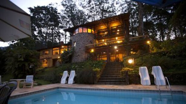 A pool area with lounge chairs and a stone structure with multiple windows and lights. - Bromelia Sabia & Cia (Teresópolis)