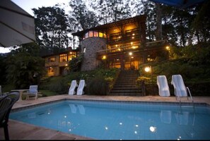 A pool area with lounge chairs and a stone structure with multiple windows and lights.