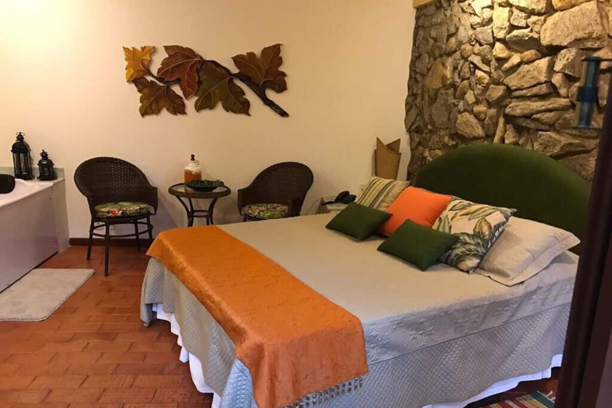 A bedroom with a bed, two chairs, a small table, a stone wall, and autumn leaves decoration.