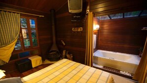 A cozy cabin room with a bed, a television, a fireplace, and a hot tub. - Bromelia Sabia & Cia (Teresópolis)
